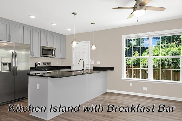 kitchen with hardwood / wood-style floors, stainless steel appliances, decorative light fixtures, and kitchen peninsula