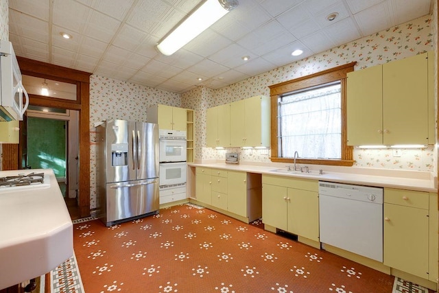 kitchen featuring a sink, white appliances, light countertops, and wallpapered walls