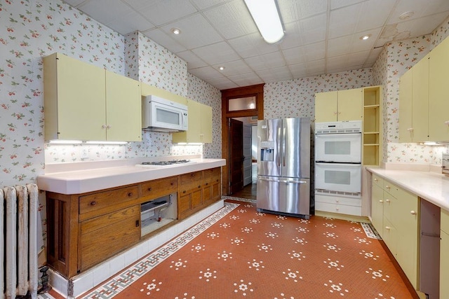 kitchen with light countertops, radiator heating unit, white appliances, a drop ceiling, and wallpapered walls