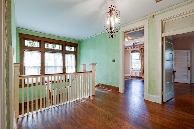 empty room featuring radiator, an inviting chandelier, baseboards, and wood finished floors