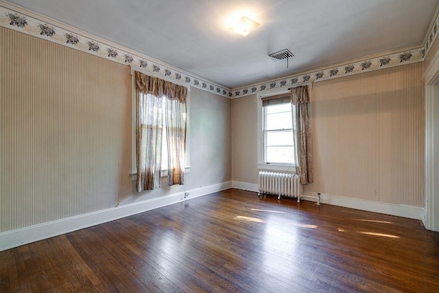 unfurnished room with radiator, visible vents, baseboards, and hardwood / wood-style floors