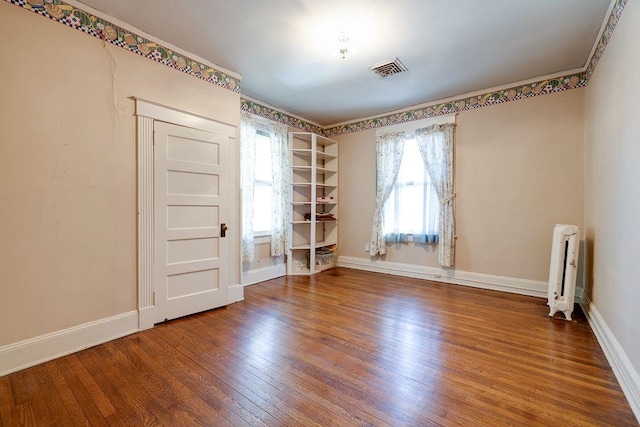 spare room with hardwood / wood-style flooring, radiator, visible vents, and baseboards