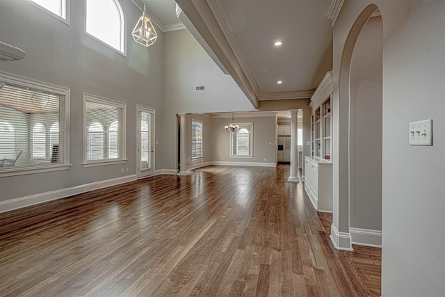 unfurnished living room featuring ornate columns, crown molding, wood-type flooring, and a chandelier