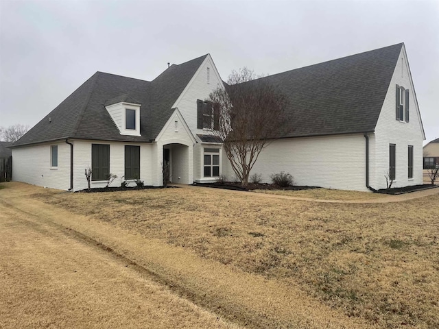 view of front of property with roof with shingles, a front yard, and brick siding