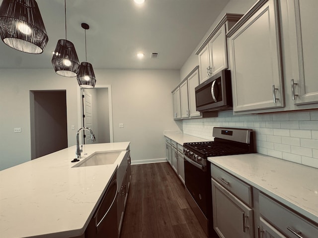 kitchen featuring gray cabinetry, stainless steel appliances, a sink, light stone countertops, and decorative light fixtures