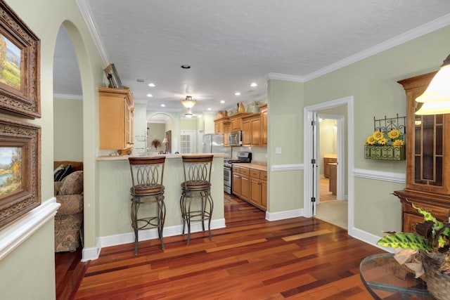 kitchen with stainless steel appliances, a peninsula, dark wood finished floors, ornamental molding, and a kitchen bar