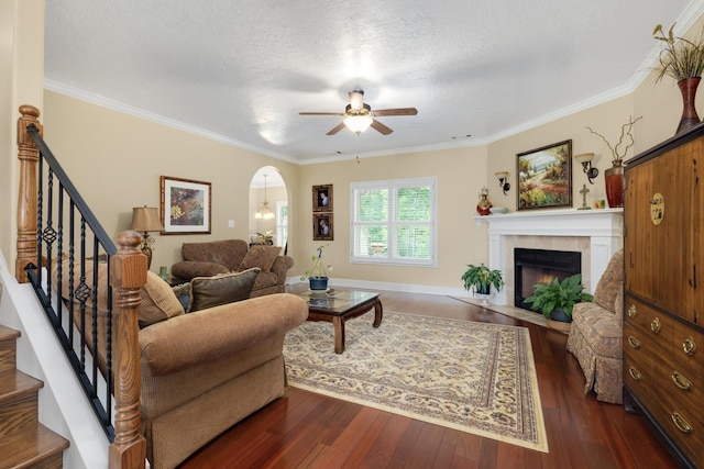 living room featuring crown molding, a tiled fireplace, arched walkways, and dark wood-type flooring