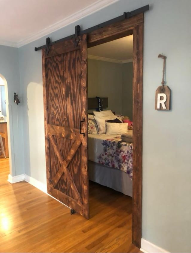 bedroom featuring crown molding, a barn door, and wood-type flooring