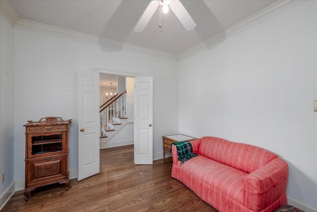 living area featuring dark wood-type flooring, ceiling fan with notable chandelier, and crown molding