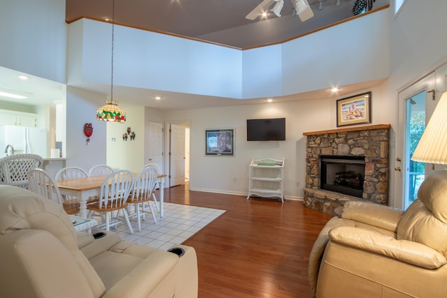 living room featuring a high ceiling, ceiling fan, a stone fireplace, and wood-type flooring