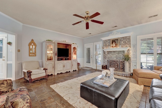 tiled living room featuring ceiling fan, a textured ceiling, a brick fireplace, and crown molding