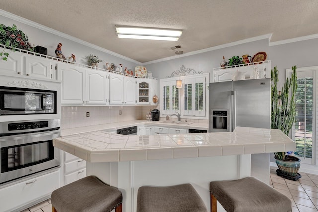 kitchen with stainless steel appliances, light tile patterned floors, a kitchen bar, and tile counters