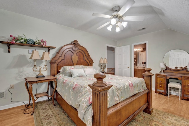 bedroom with ensuite bath, light hardwood / wood-style floors, a textured ceiling, ceiling fan, and lofted ceiling