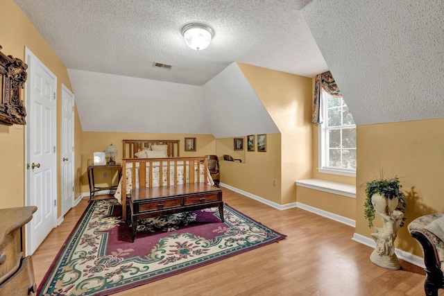 bedroom featuring light wood-type flooring, a textured ceiling, and lofted ceiling