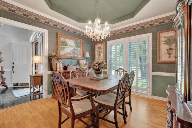 dining area with hardwood / wood-style floors, a raised ceiling, ornamental molding, and a chandelier