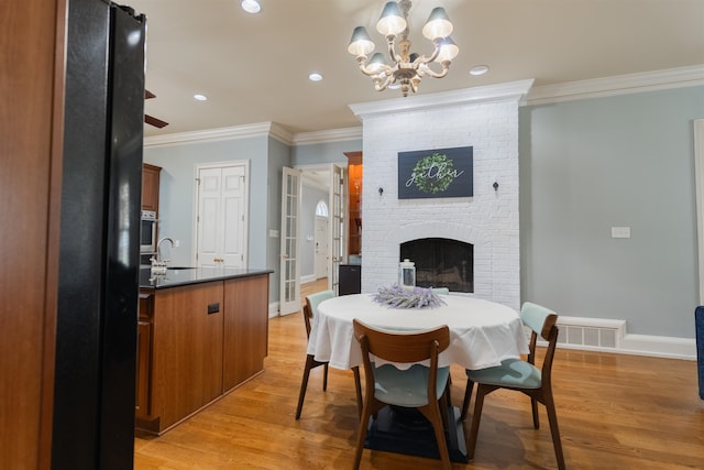 dining room featuring a fireplace, light wood-type flooring, sink, and crown molding