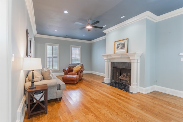 living room with light hardwood / wood-style flooring, ceiling fan, ornamental molding, and a premium fireplace