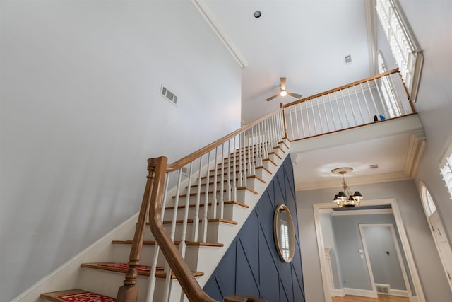 staircase featuring ceiling fan with notable chandelier, a towering ceiling, and crown molding