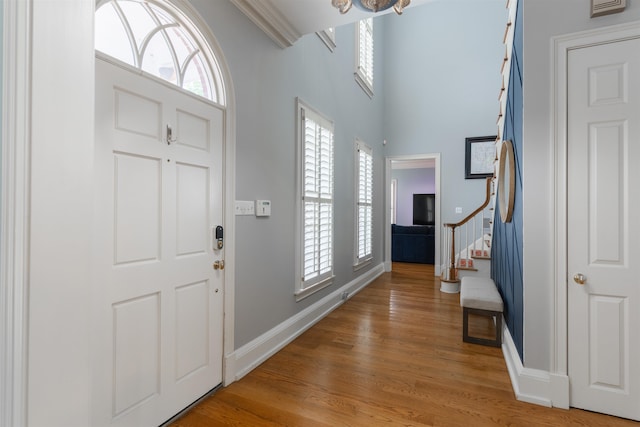 entryway with a towering ceiling, ornamental molding, and wood-type flooring