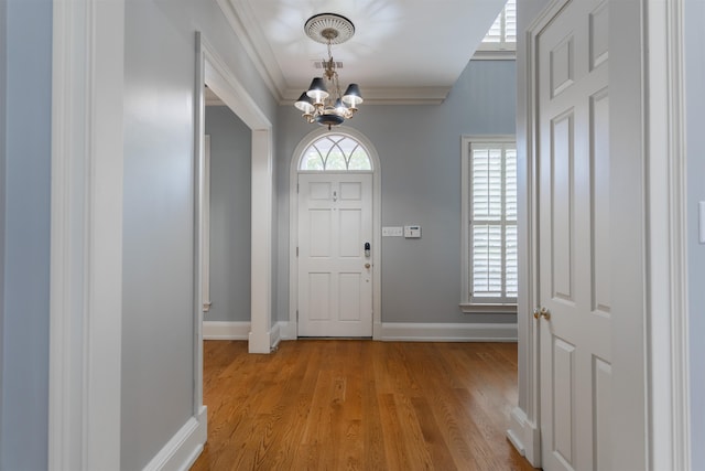 entryway with ornamental molding, an inviting chandelier, and light wood-type flooring