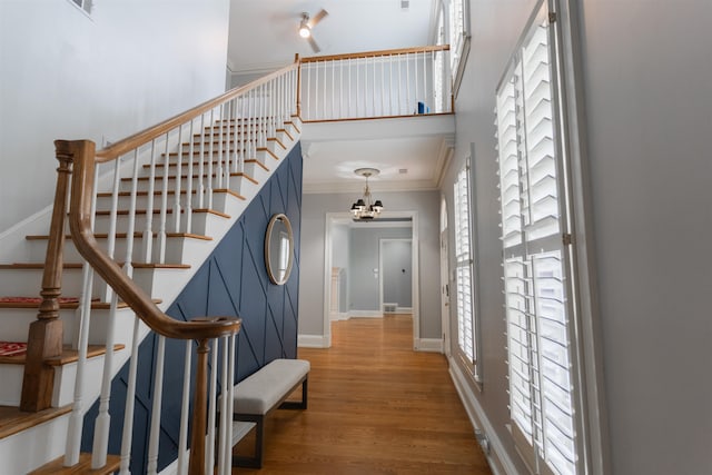 stairs with hardwood / wood-style flooring, an inviting chandelier, a towering ceiling, and ornamental molding