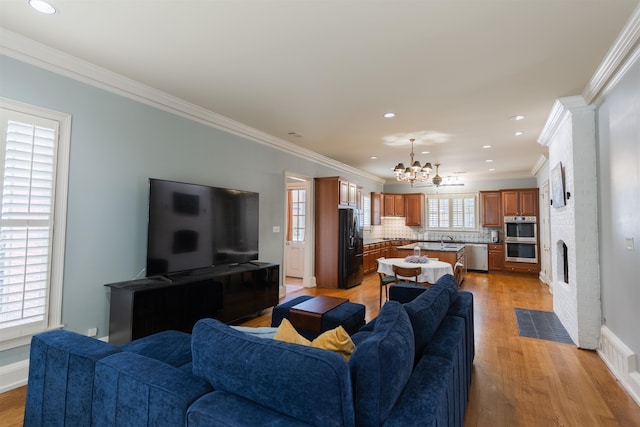 living room featuring light wood-type flooring, crown molding, a brick fireplace, and an inviting chandelier