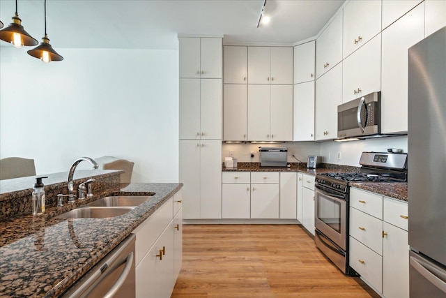 kitchen featuring light wood-type flooring, pendant lighting, track lighting, white cabinetry, and stainless steel appliances