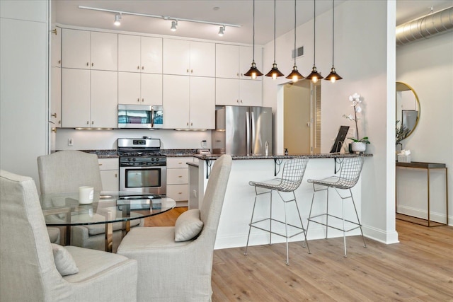 kitchen with light wood-type flooring, pendant lighting, white cabinets, track lighting, and stainless steel appliances