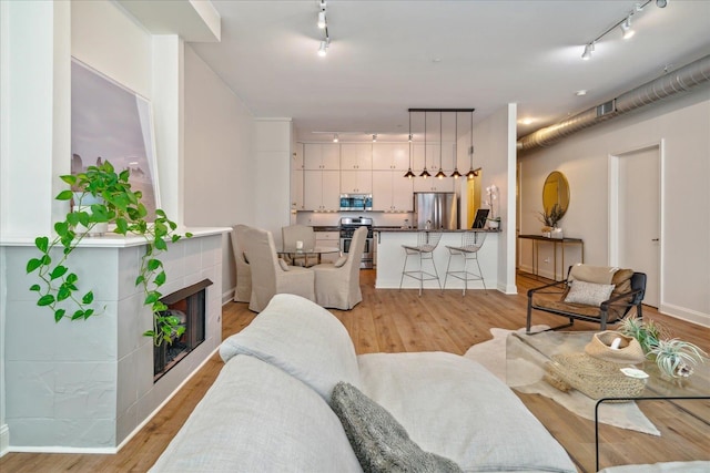 living room with rail lighting, light hardwood / wood-style flooring, and a tile fireplace