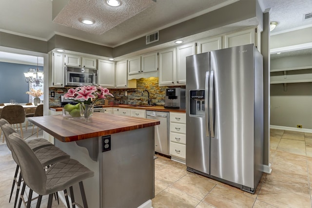 kitchen featuring tasteful backsplash, visible vents, butcher block countertops, stainless steel appliances, and a textured ceiling