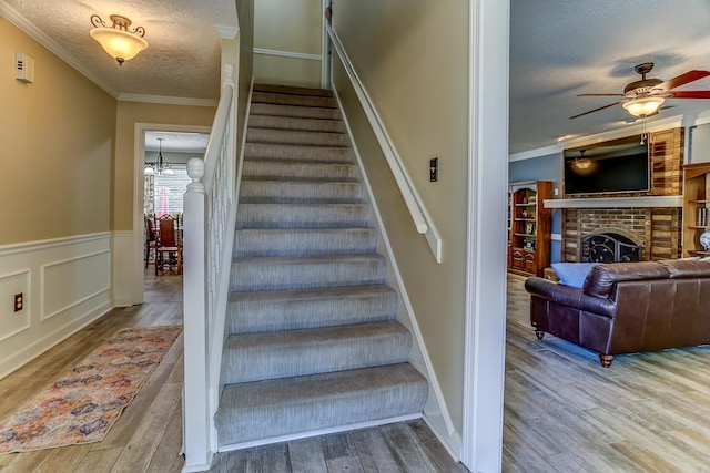 staircase with a fireplace, a textured ceiling, ceiling fan with notable chandelier, and hardwood / wood-style floors