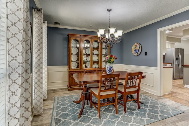 dining space with an inviting chandelier, light hardwood / wood-style flooring, a textured ceiling, and ornamental molding