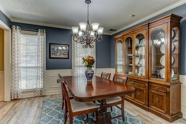 dining room with a textured ceiling, a notable chandelier, light hardwood / wood-style floors, and ornamental molding