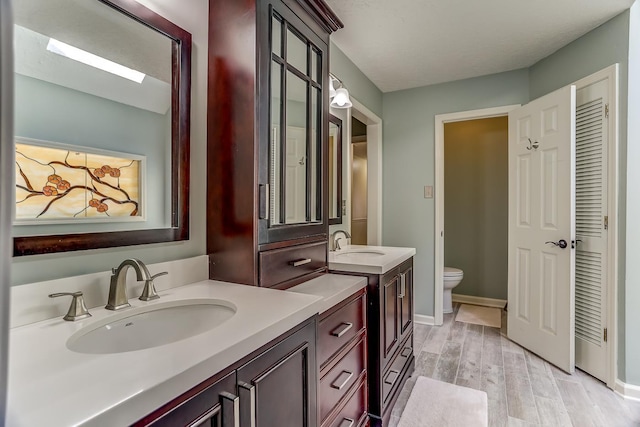 full bath with wood finished floors, two vanities, a sink, and toilet