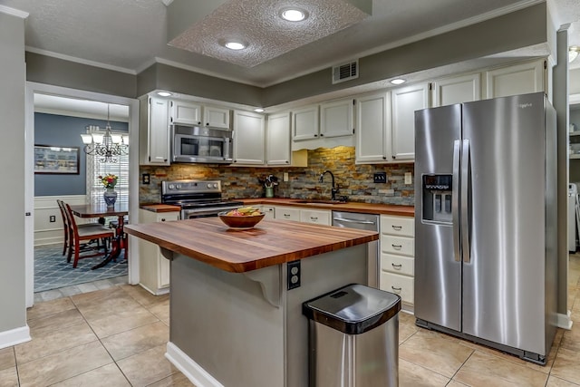 kitchen with decorative backsplash, appliances with stainless steel finishes, butcher block counters, and light tile patterned floors