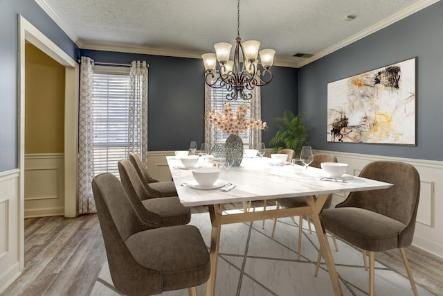 dining room featuring a wainscoted wall, a textured ceiling, ornamental molding, and wood finished floors