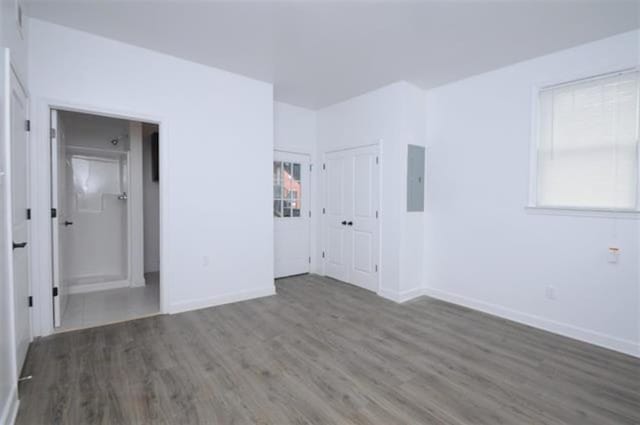 unfurnished bedroom with baseboards, multiple windows, wood finished floors, and electric panel
