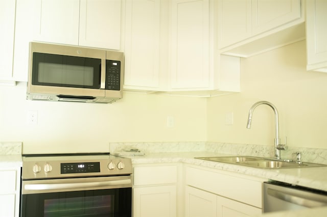 kitchen featuring white cabinetry, stainless steel appliances, a sink, and light countertops