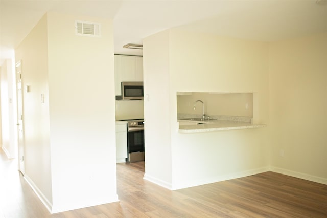 interior space with light wood-style flooring, a sink, visible vents, and baseboards