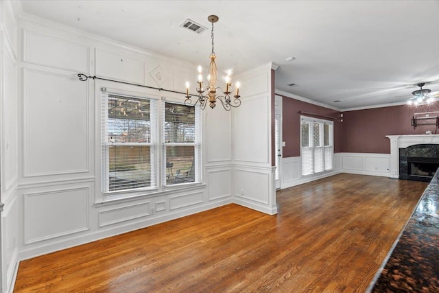 unfurnished dining area with a fireplace, visible vents, a decorative wall, wood finished floors, and ceiling fan with notable chandelier