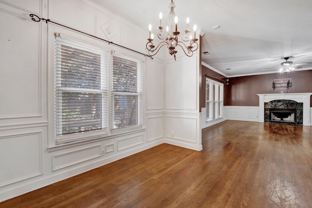 unfurnished dining area with a high end fireplace, ceiling fan with notable chandelier, dark wood-type flooring, and ornamental molding