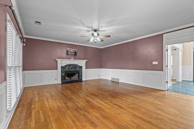 unfurnished living room featuring a high end fireplace, visible vents, ceiling fan, and wood finished floors