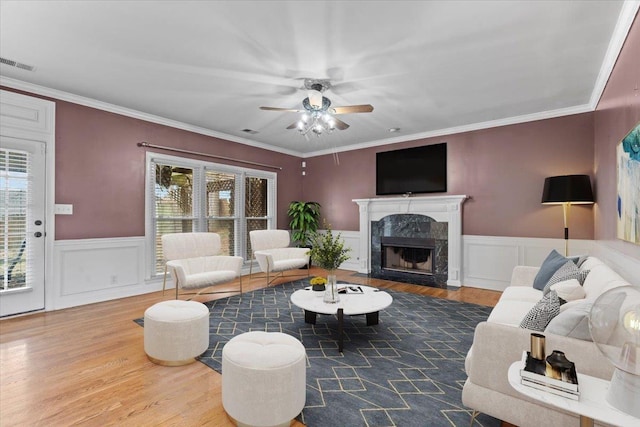 living room featuring visible vents, wainscoting, a premium fireplace, ornamental molding, and wood finished floors