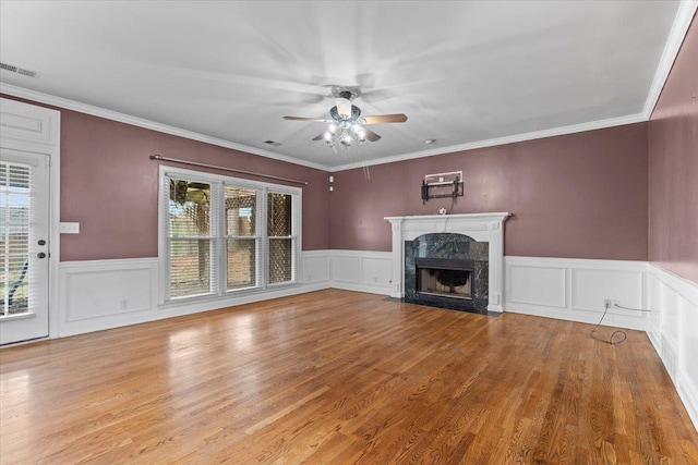 unfurnished living room featuring ceiling fan, a wainscoted wall, a fireplace, wood finished floors, and visible vents