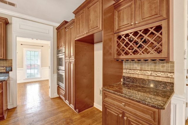 kitchen with decorative backsplash, light wood-type flooring, dark stone countertops, crown molding, and double oven