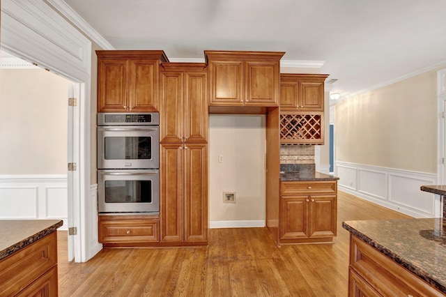 kitchen with double oven, light hardwood / wood-style floors, and dark stone counters