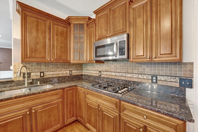 kitchen with stainless steel appliances, ornamental molding, sink, light wood-type flooring, and dark stone counters