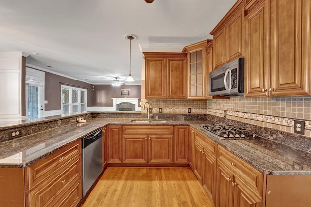 kitchen featuring appliances with stainless steel finishes, light hardwood / wood-style flooring, decorative light fixtures, sink, and dark stone countertops