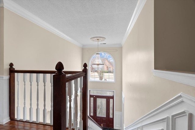 foyer with a textured ceiling, wainscoting, a notable chandelier, and crown molding