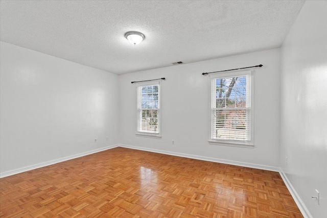 spare room featuring visible vents, a healthy amount of sunlight, a textured ceiling, and baseboards